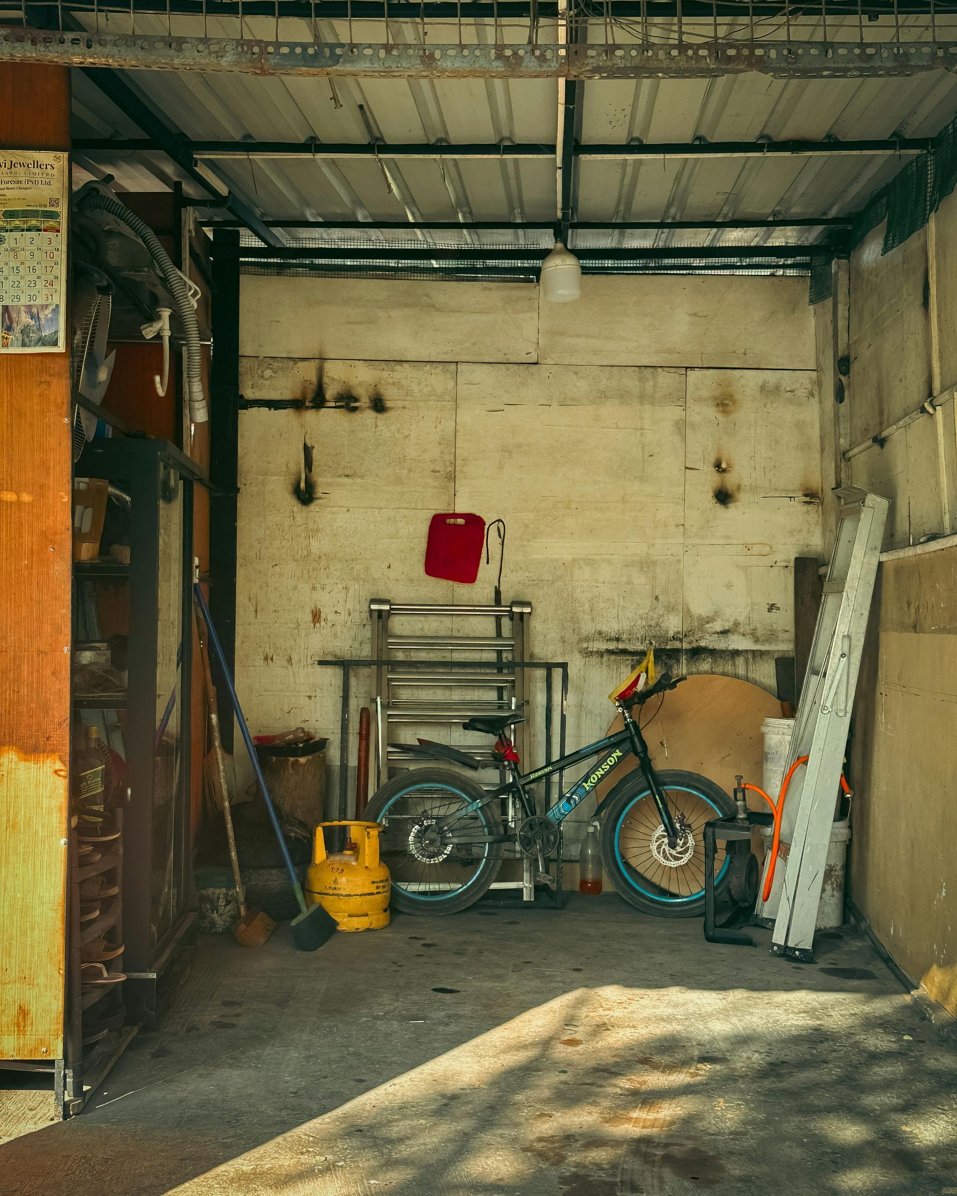 Cluttered garage with a bicycle, tools, and a yellow gas can against a worn wall.