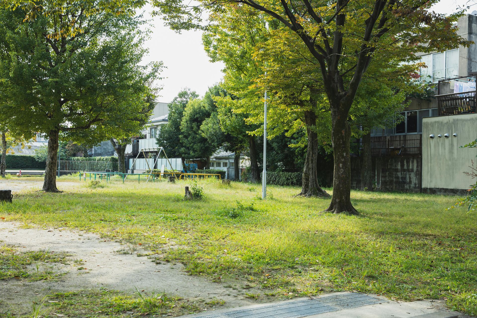 Quiet grassy park with trees, a dirt path, and a building in the background