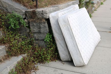 Two discarded mattresses leaning against a stone wall on a sidewalk