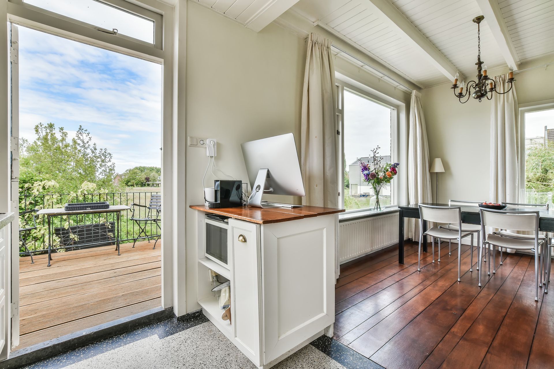 Bright dining nook with open doors to a patio, white cabinets, wood floor, and chandelier.