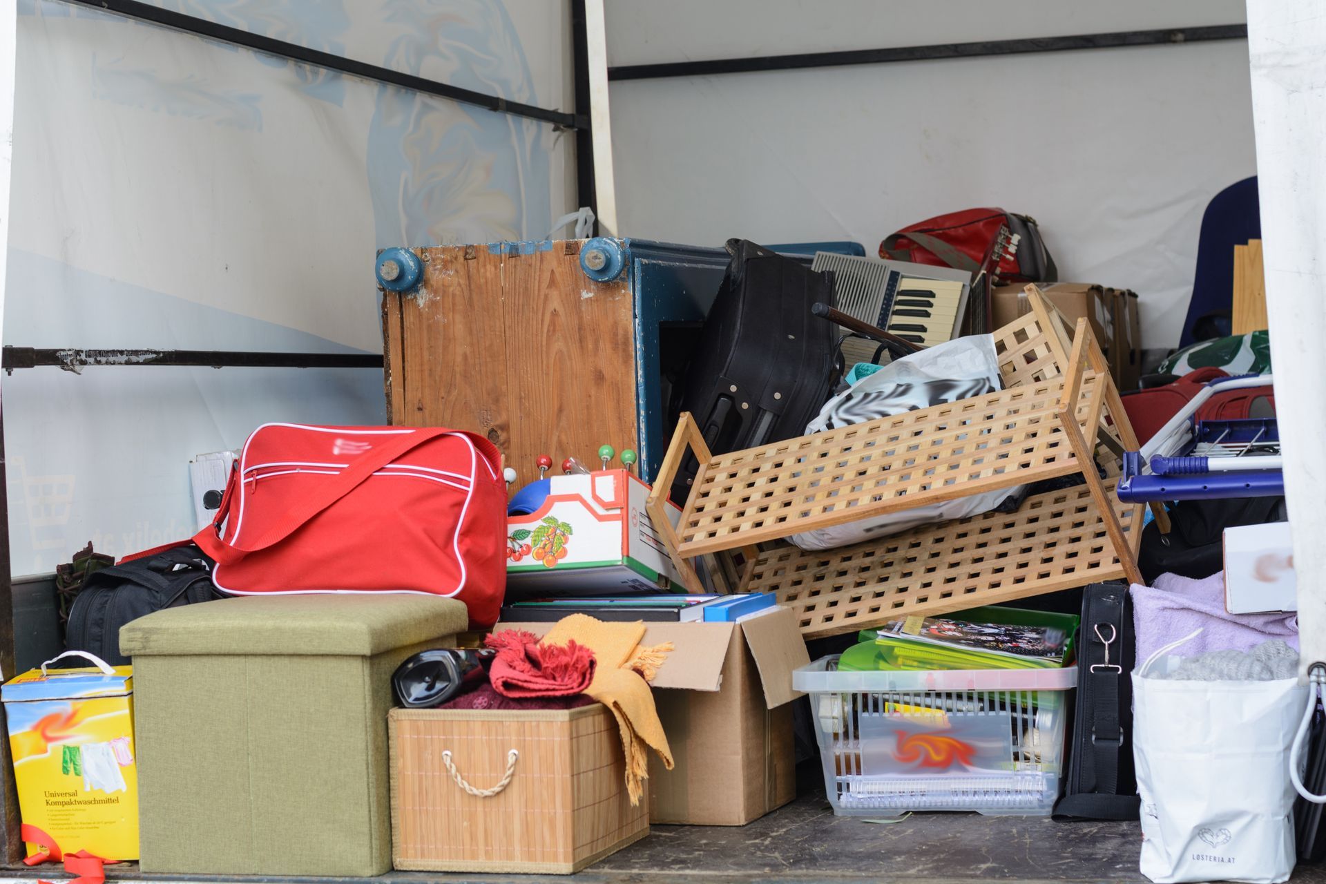 Packed moving truck with stacked boxes, bins, bags, and a wicker basket under a white cargo roof