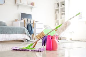 Cleaning supplies and mop in a bright bedroom with a bed and desk in the background