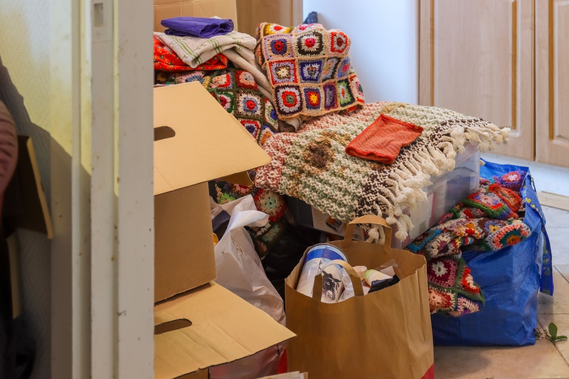 Cluttered room with stacked moving boxes, blankets, and bags of assorted household items.