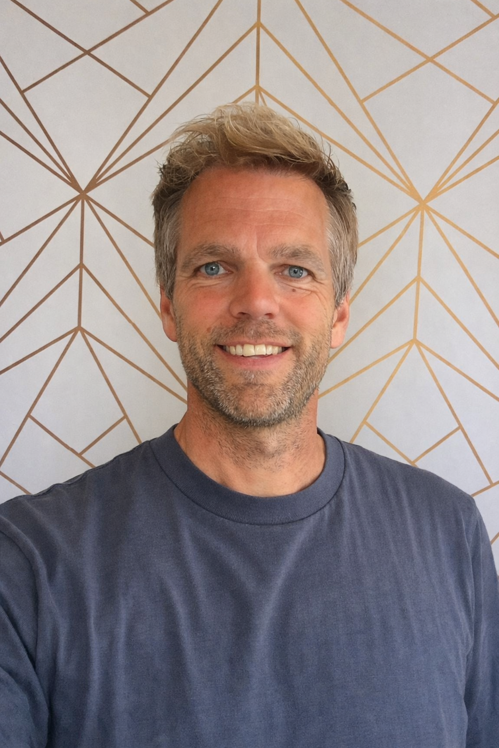 Man met bril, lichtblauwe jas over een donkerblauw overhemd, handen in de zakken in een blauw geknipte papieren stijl