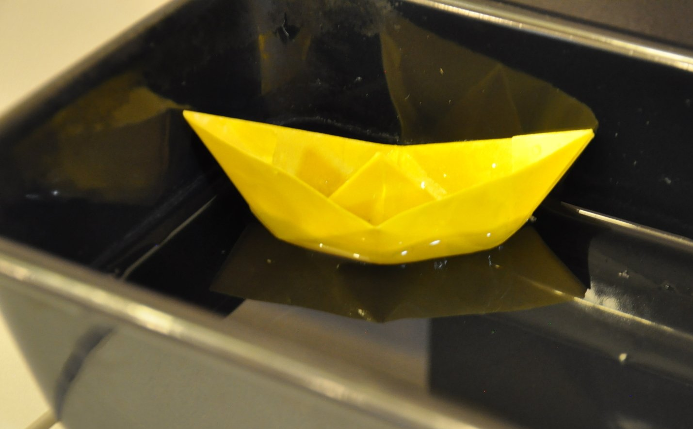 ein aus gewachstem Papier gefaltetes Boot auf Wasser in einer Backform