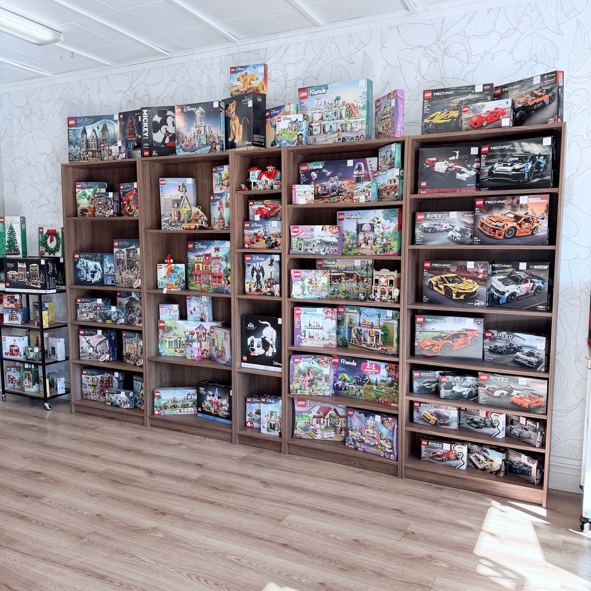Five wooden shelving units lined against a white wall, filled with numerous LEGO sets in their original boxes.