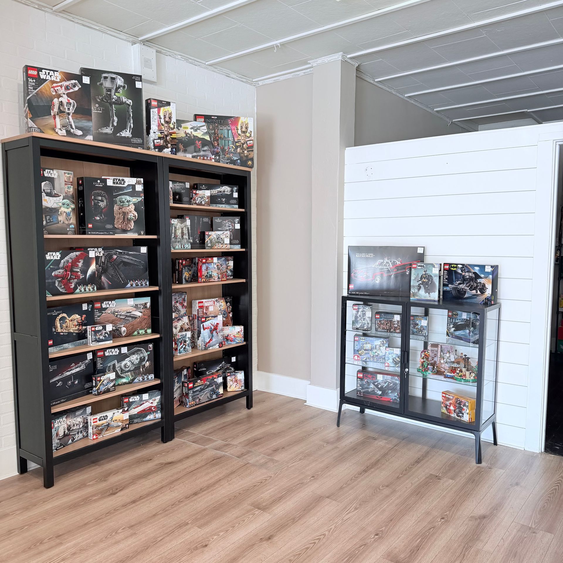 A shop interior with two black wooden shelves and a glass display case filled with boxed Lego sets on a wood floor.