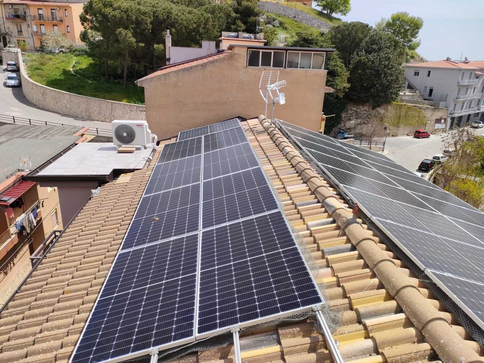 Pannelli solari installati su un tetto di tegole di terracotta con edifici e una strada sullo sfondo.