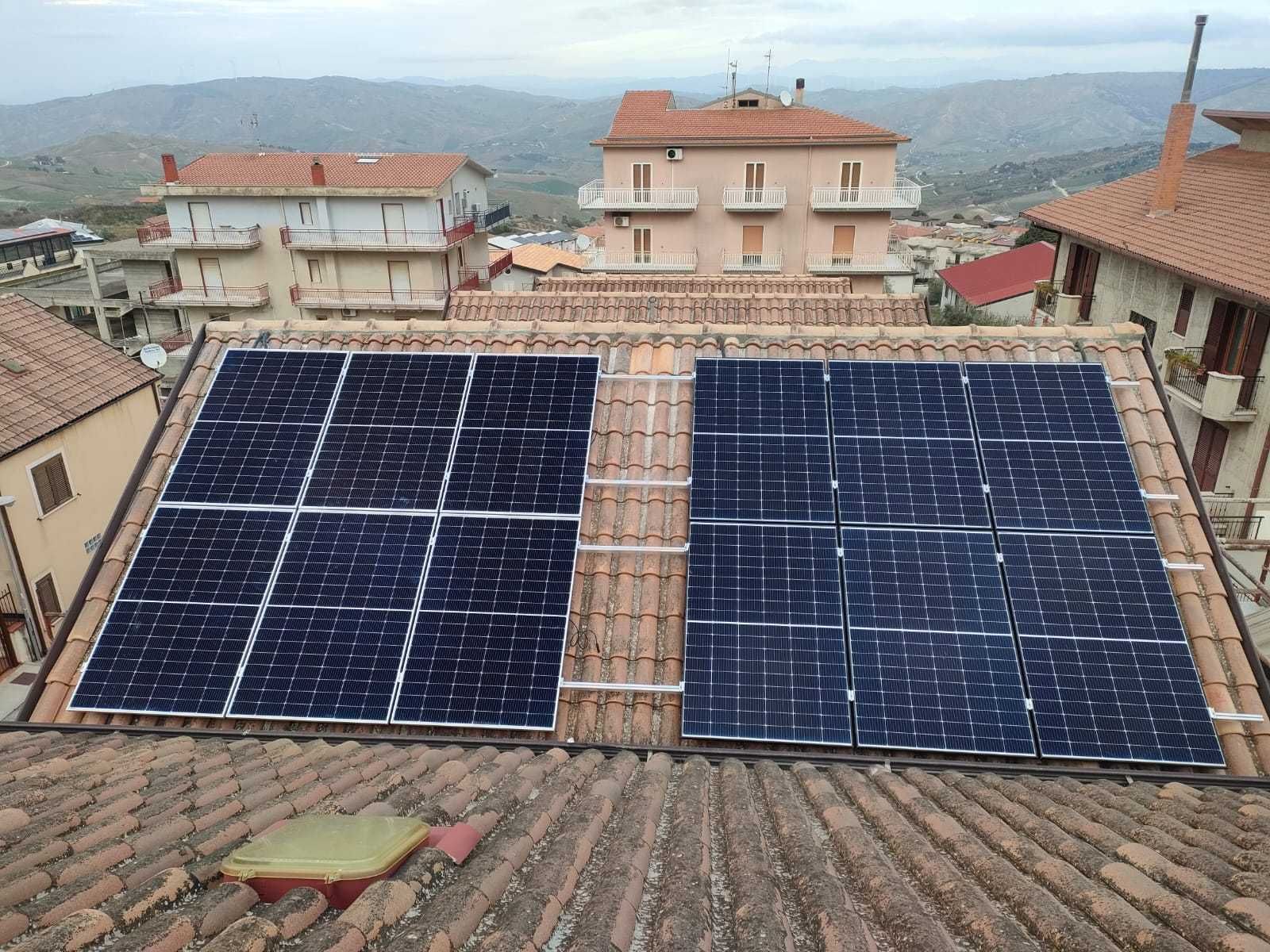 Pannelli solari su un tetto di tegole in una città, con edifici e colline sullo sfondo.
