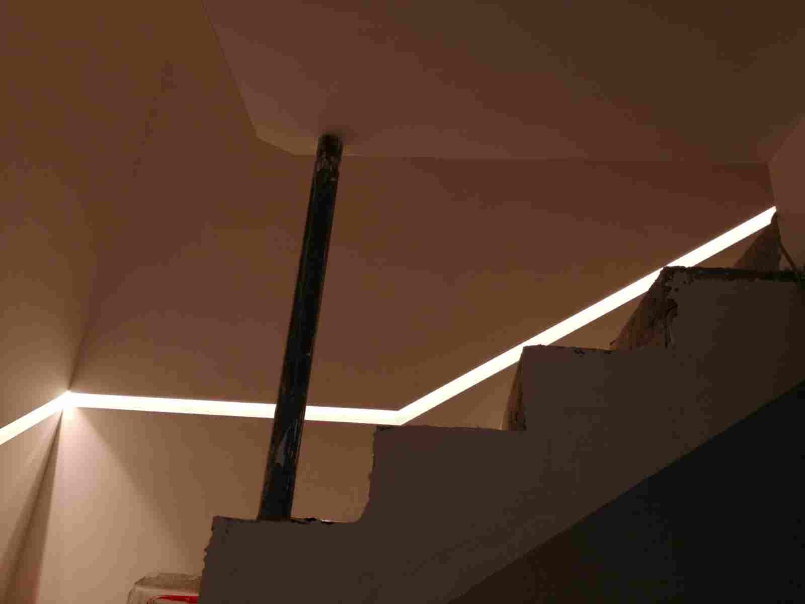 Scala con illuminazione a incasso. Un palo scuro corre verticalmente. Luce calda su pareti e scale.