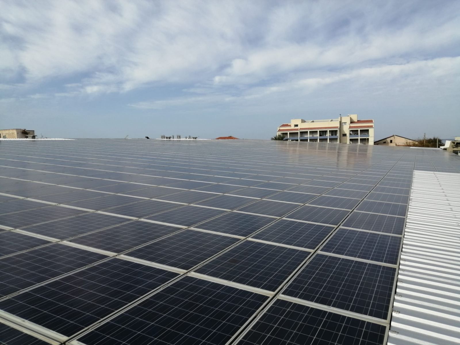 Pannelli solari sul tetto di un edificio sotto un cielo nuvoloso, con altri edifici visibili in lontananza.