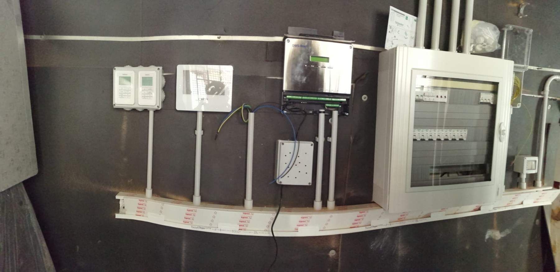 Quadri elettrici e apparecchiature montati su una parete scura, con fili e condotti visibili.