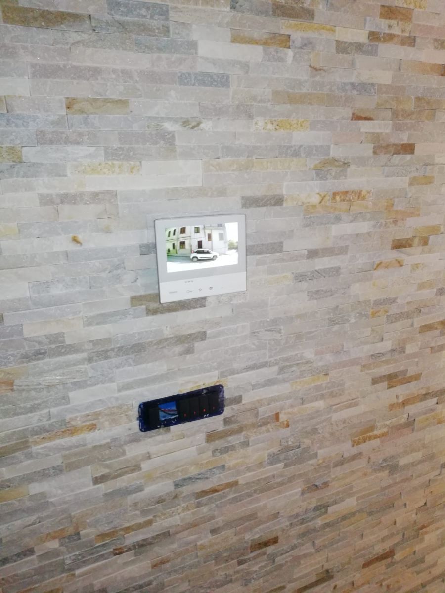 Muro con pietre accatastate. Monitor bianco che mostra l'edificio. Dispositivo nero in basso.