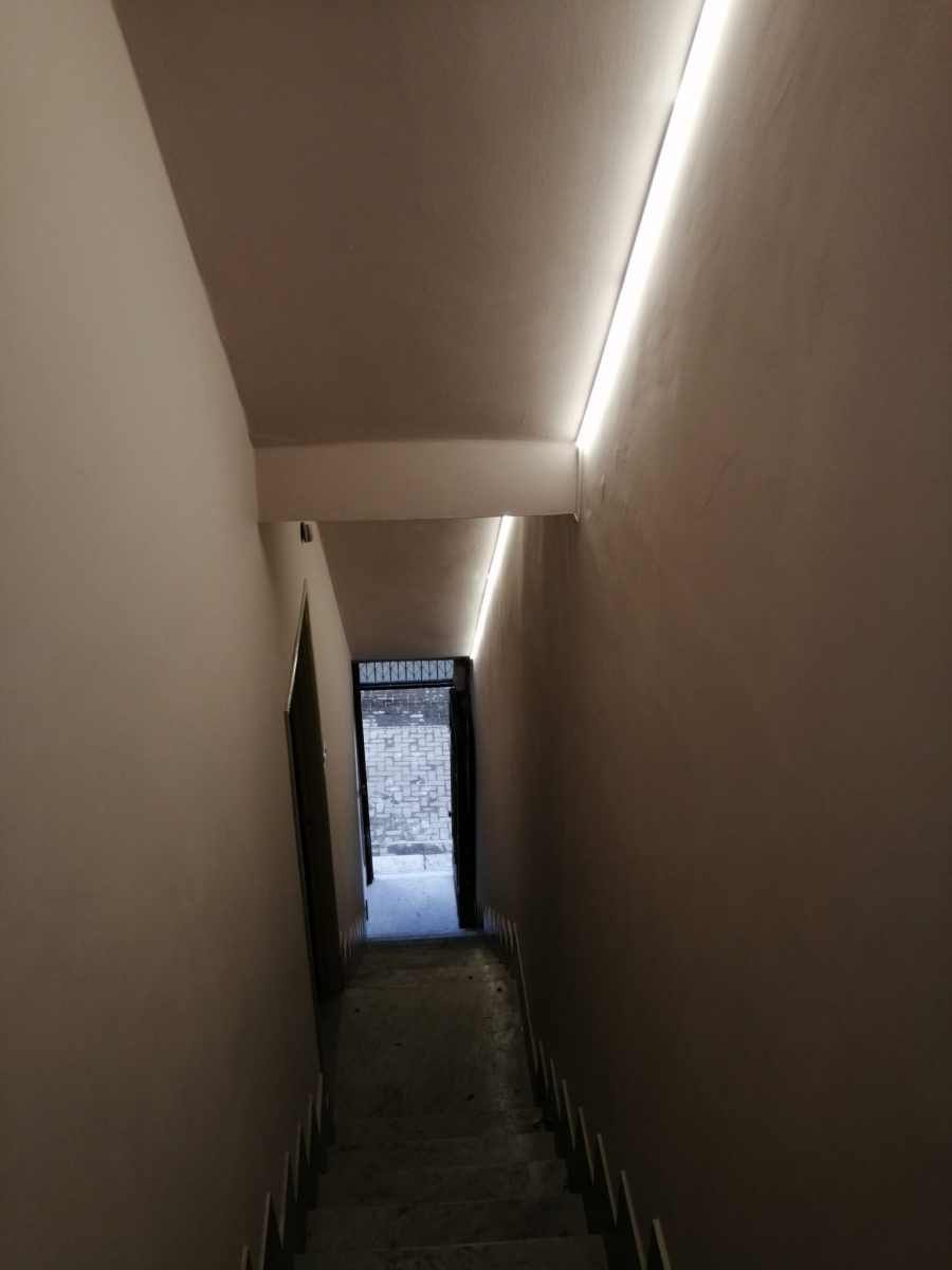 Tromba delle scale con illuminazione a strisce LED incassate nel soffitto, che conduce a una porta.