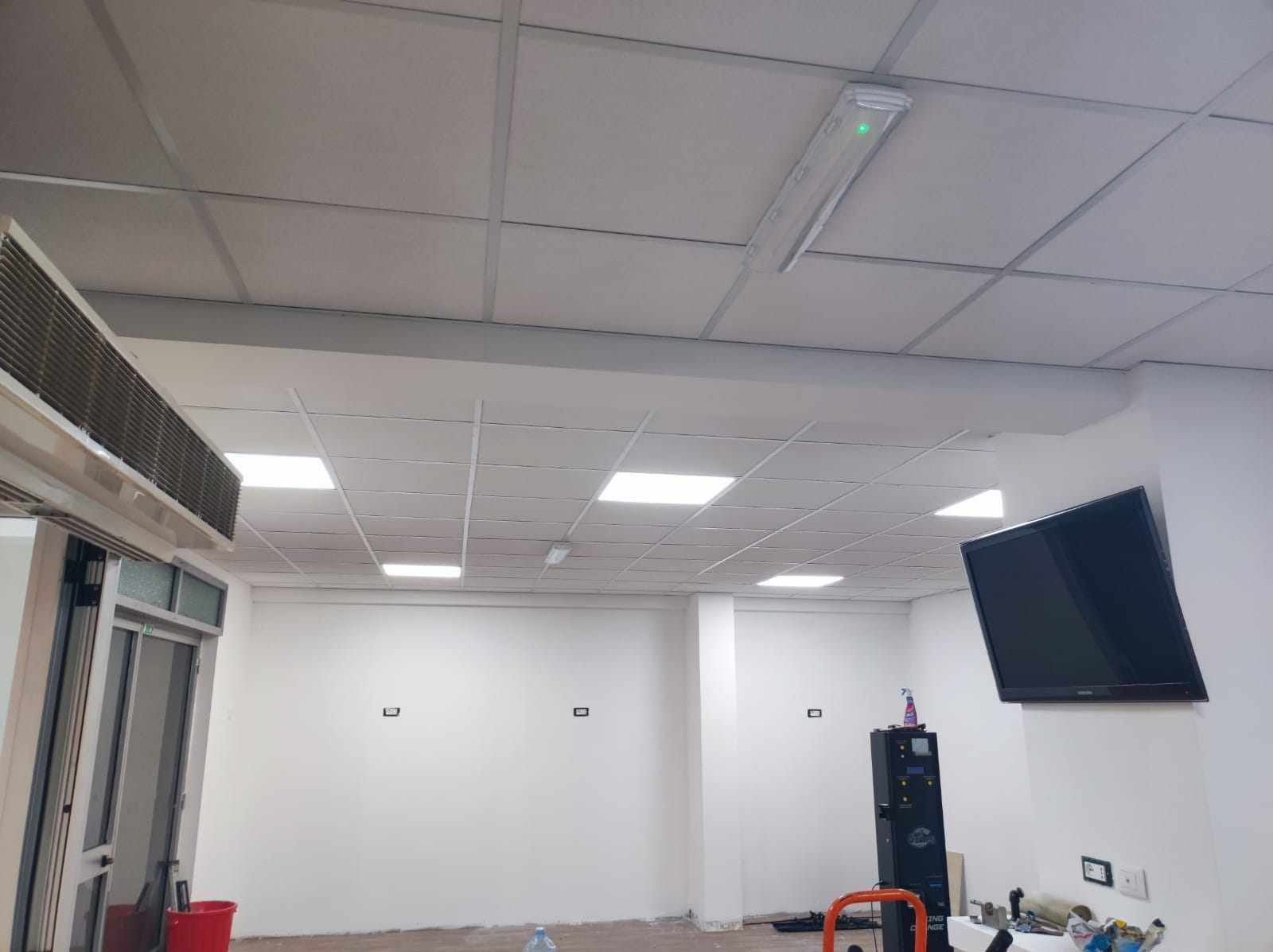 Interno con pareti bianche, TV, altoparlanti e controsoffitto con luci fluorescenti.