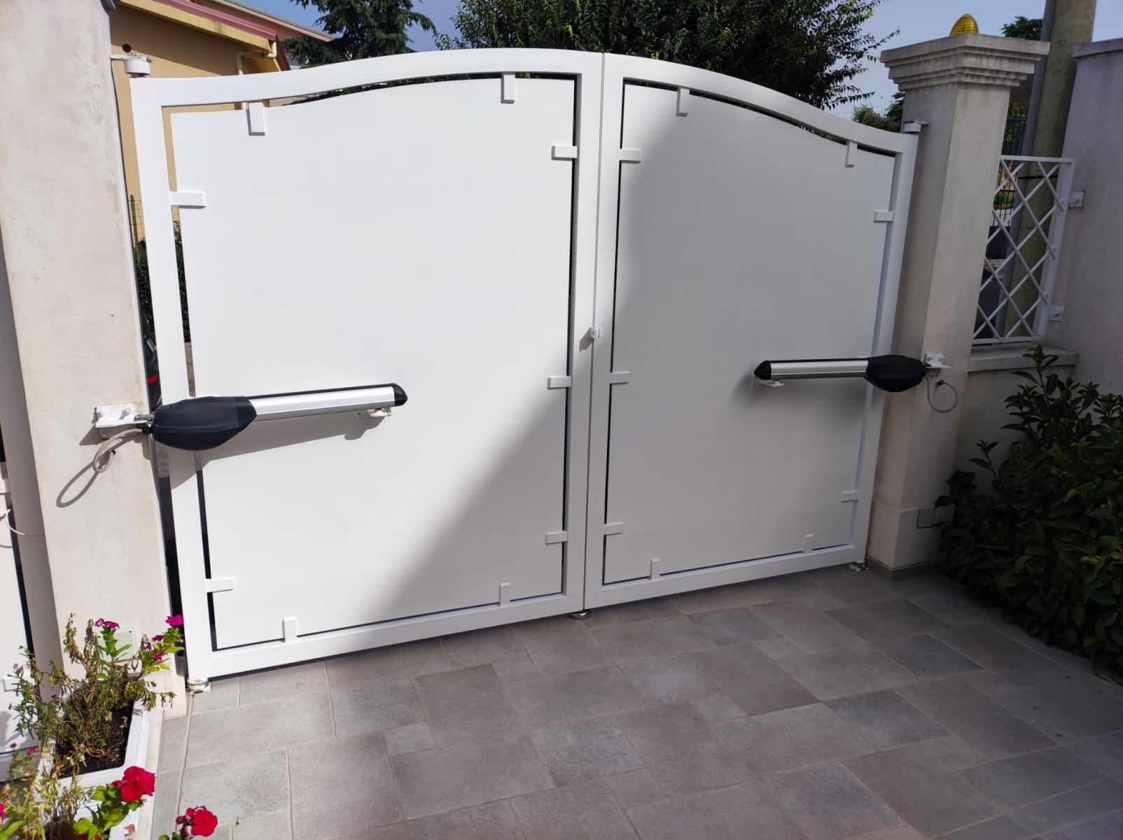 Cancello carrabile doppio bianco con apertura automatica, situato in un'area pavimentata.