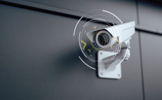 Telecamera di sicurezza montata su una parete grigia con sovrapposizione di interfaccia digitale.