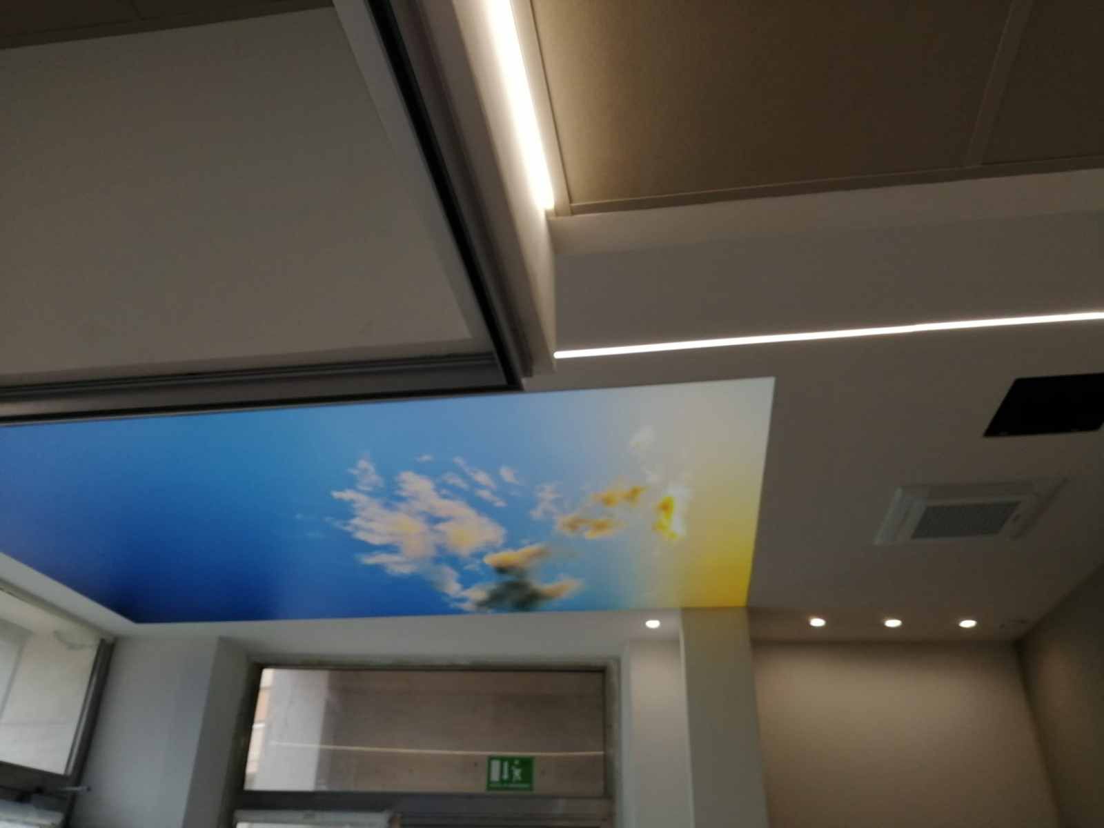Soffitto con murale raffigurante il cielo e illuminazione integrata, pareti bianche e una finestra sottostante.