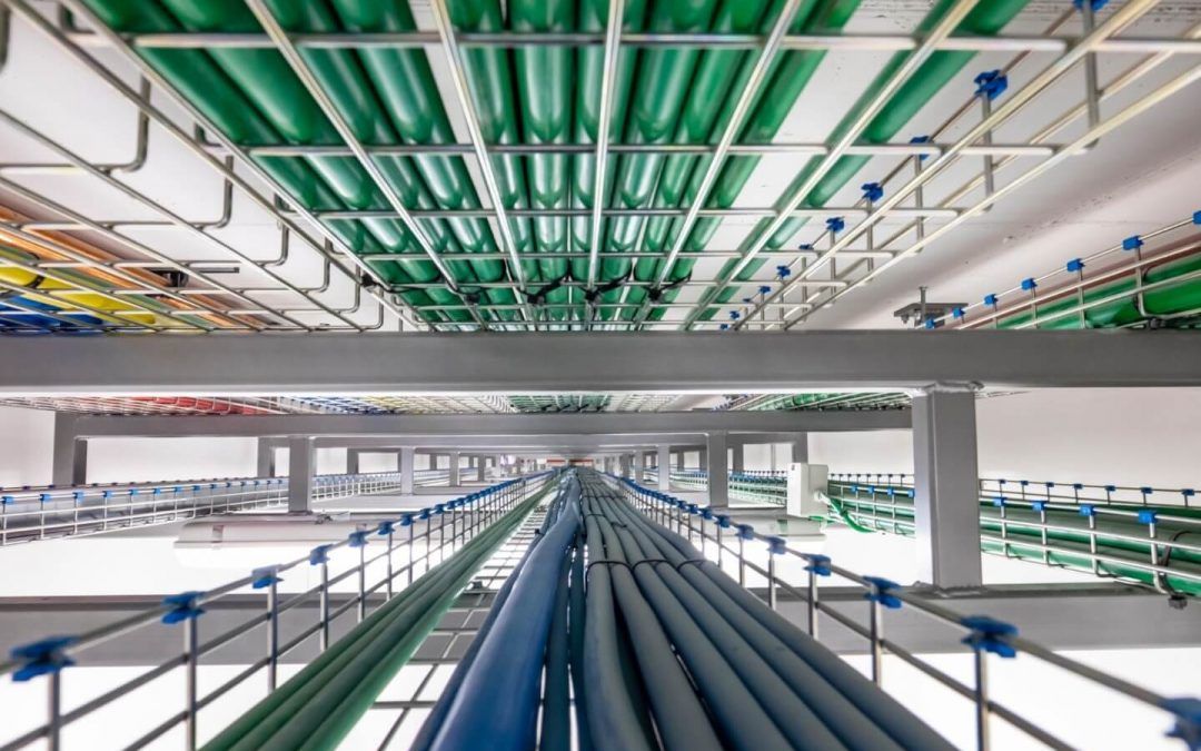 Vista dall'alto di un data center con un soffitto pieno di cavi verdi, blu e colorati che corrono lungo rack metallici.