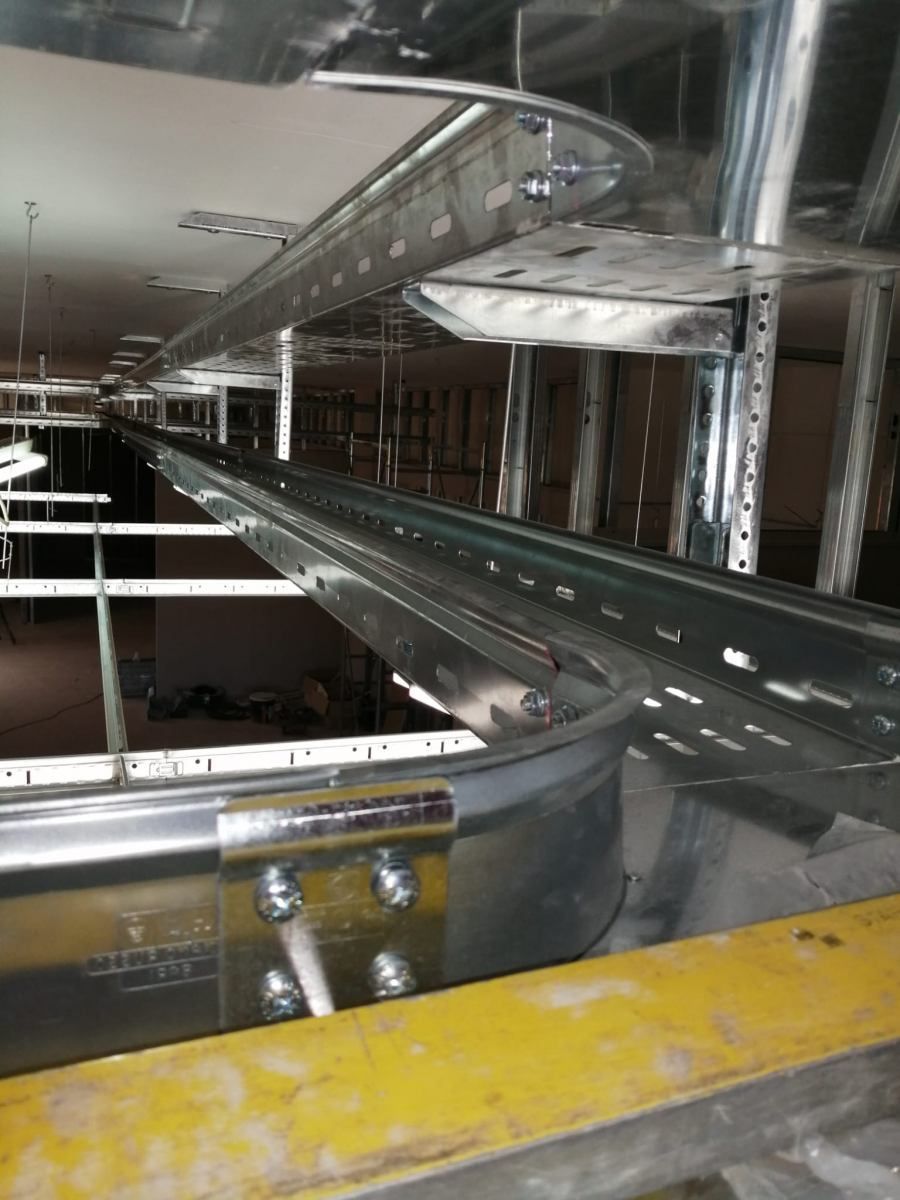 Canaline portacavi installate su un soffitto, curve in corrispondenza di una giunzione, in metallo argentato, in un ambiente industriale.