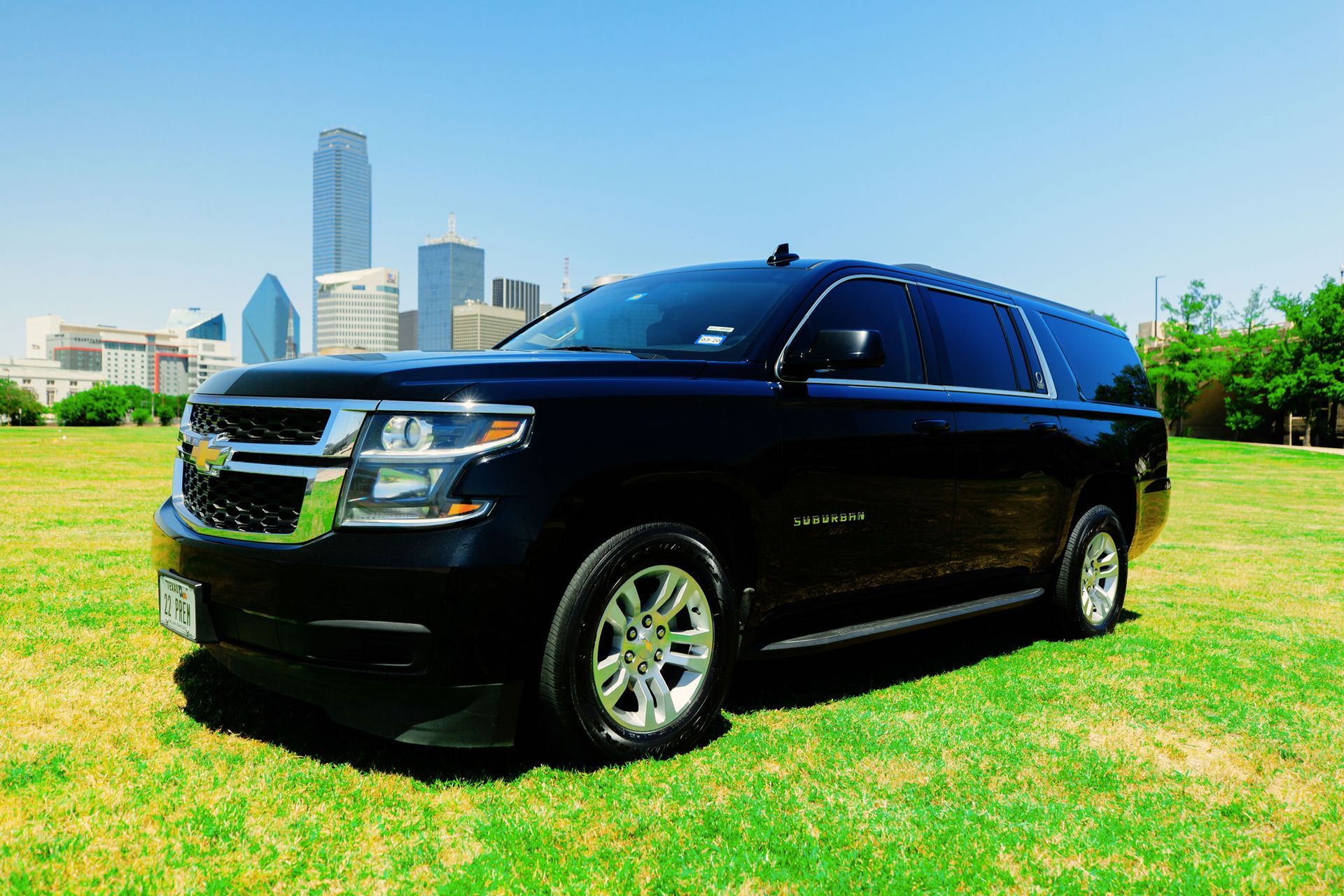 A black suv is parked in a grassy field with a city skyline in the background.