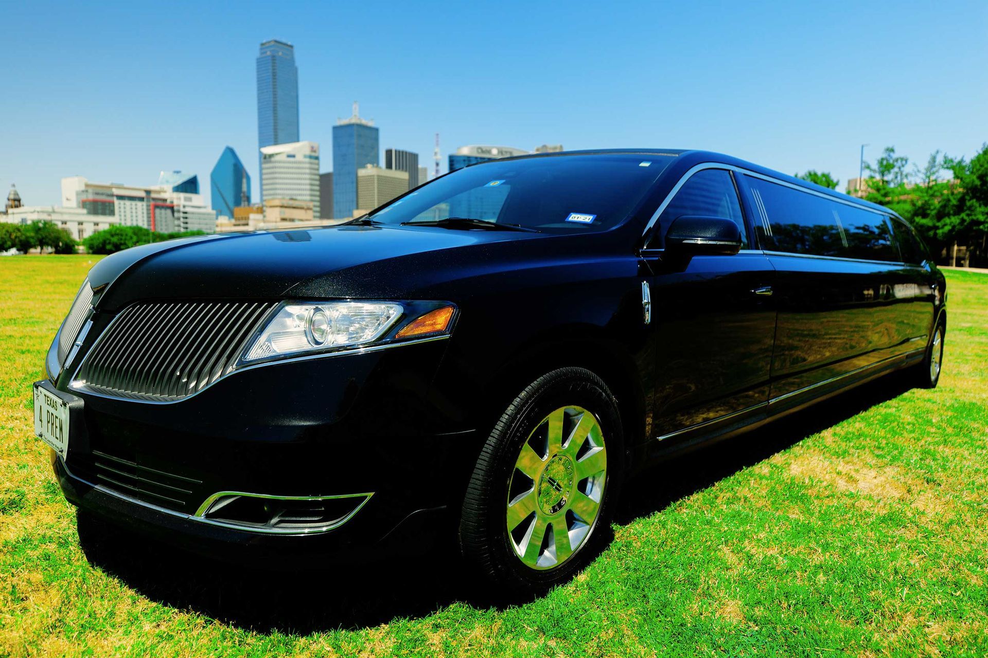 A black limousine is parked in a grassy field with a city skyline in the background