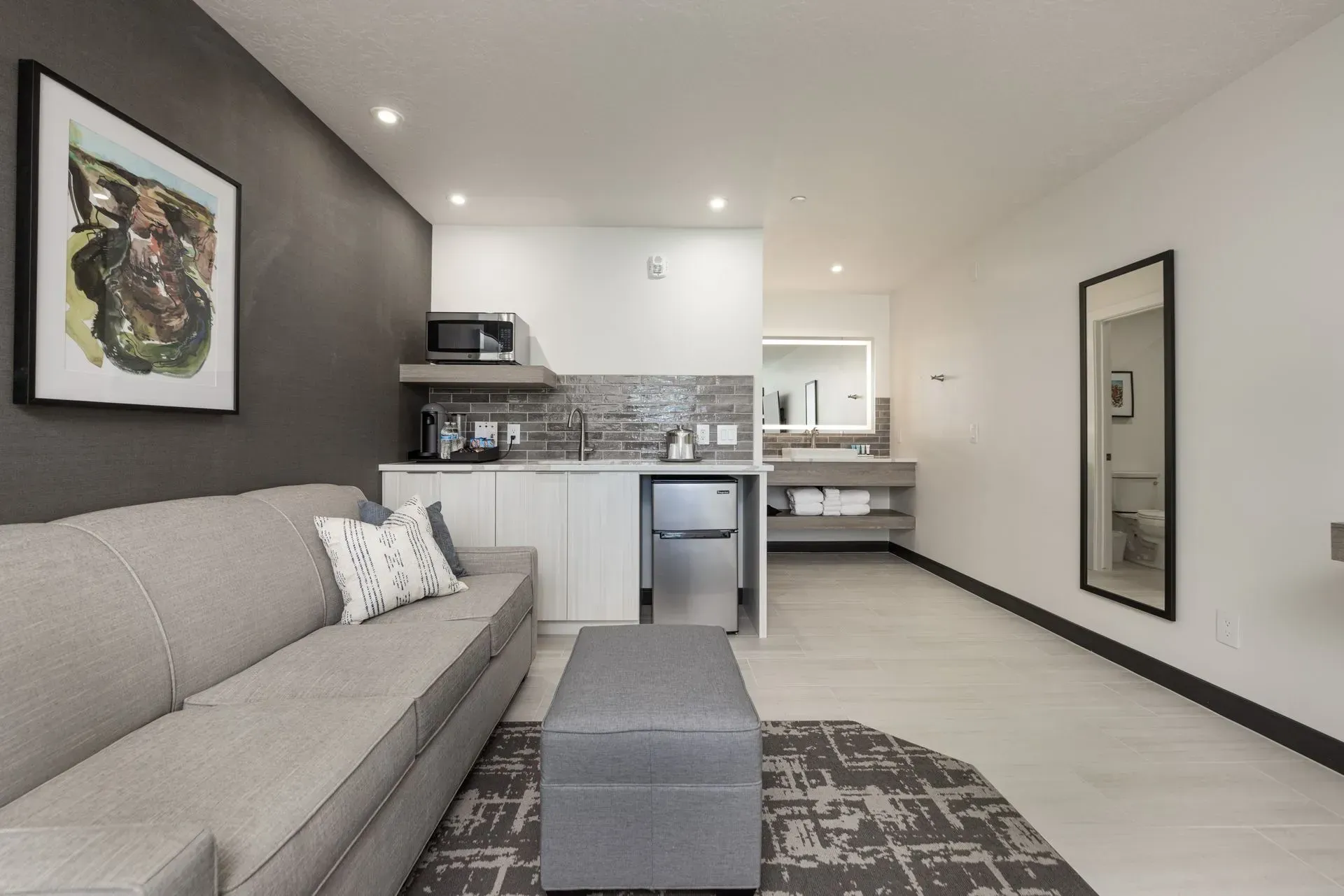 A living room with a couch and ottoman and a kitchen