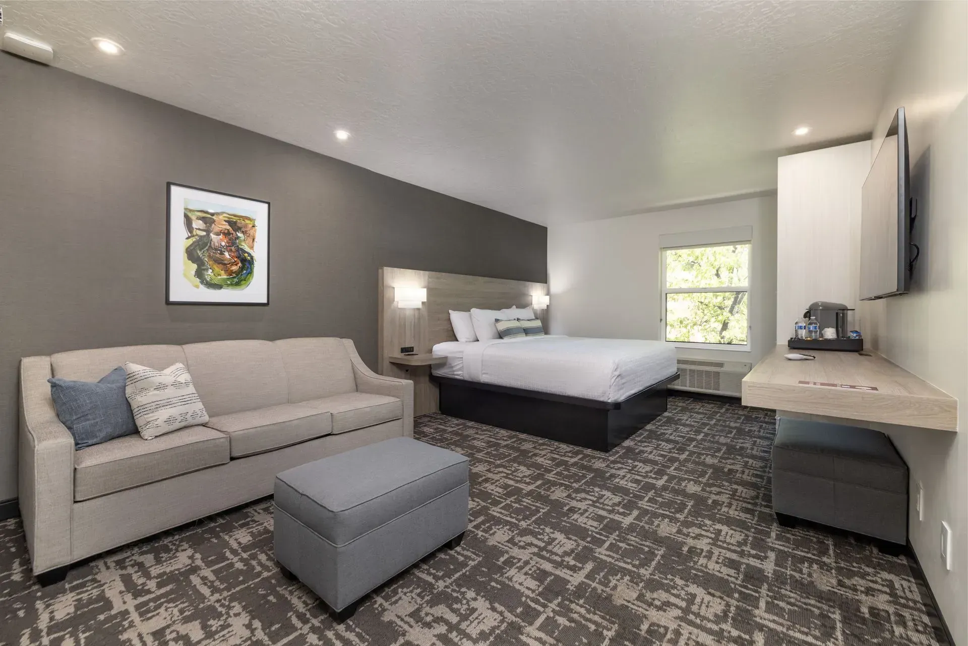 A hotel room with a king size bed , couch , ottoman and television.