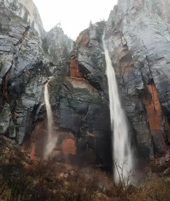 A waterfall is surrounded by rocks and trees in the middle of a canyon.
