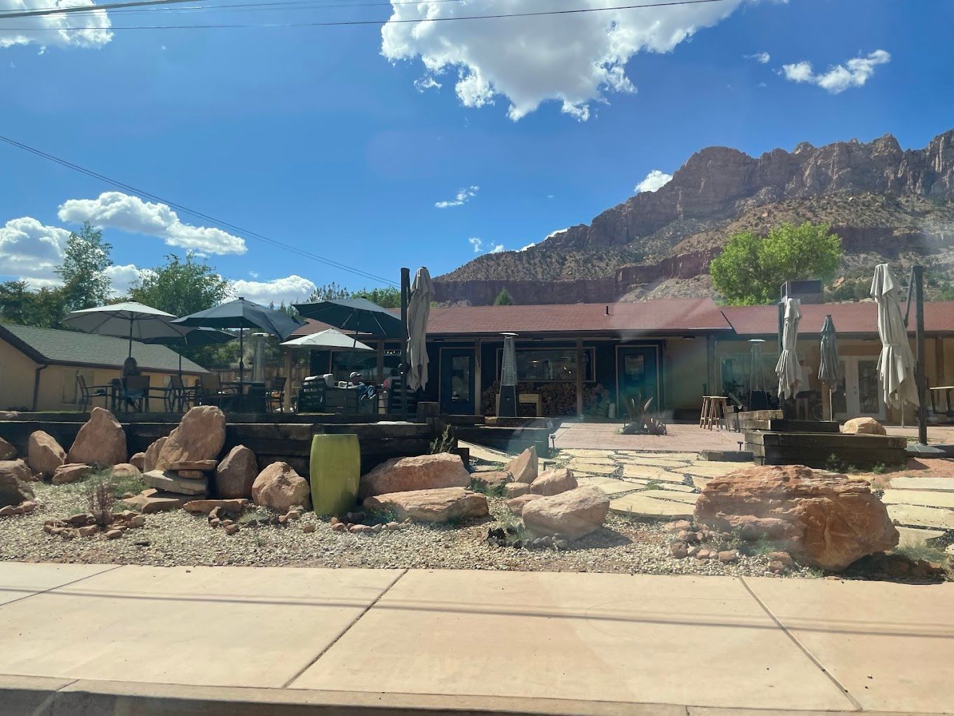 A building with a mountain in the background is surrounded by rocks and umbrellas.