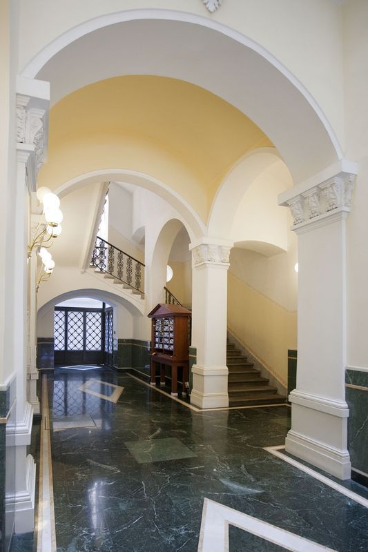 Elegante corridoio di un edificio con pavimenti in marmo, porte ad arco e una scala.