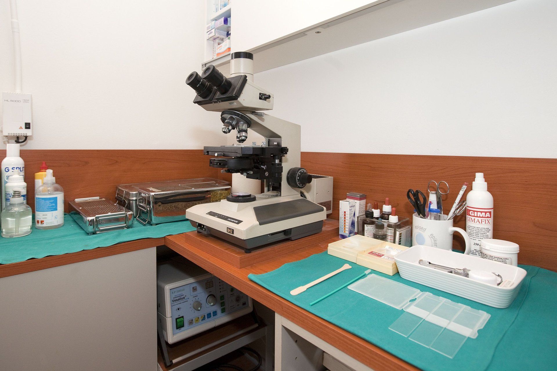 Microscopio su un banco da laboratorio con vetrini, materiali e strumenti.