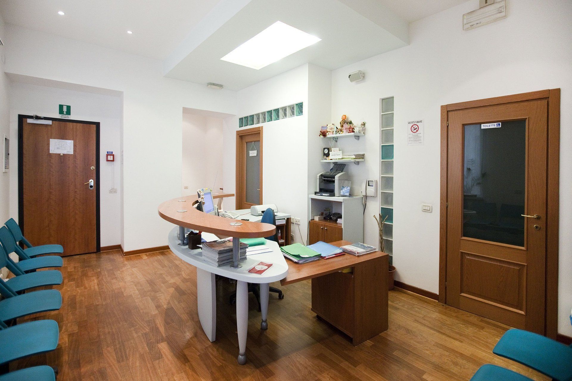 Area di accoglienza di uno studio medico con scrivania curva, sedie e due porte in legno.