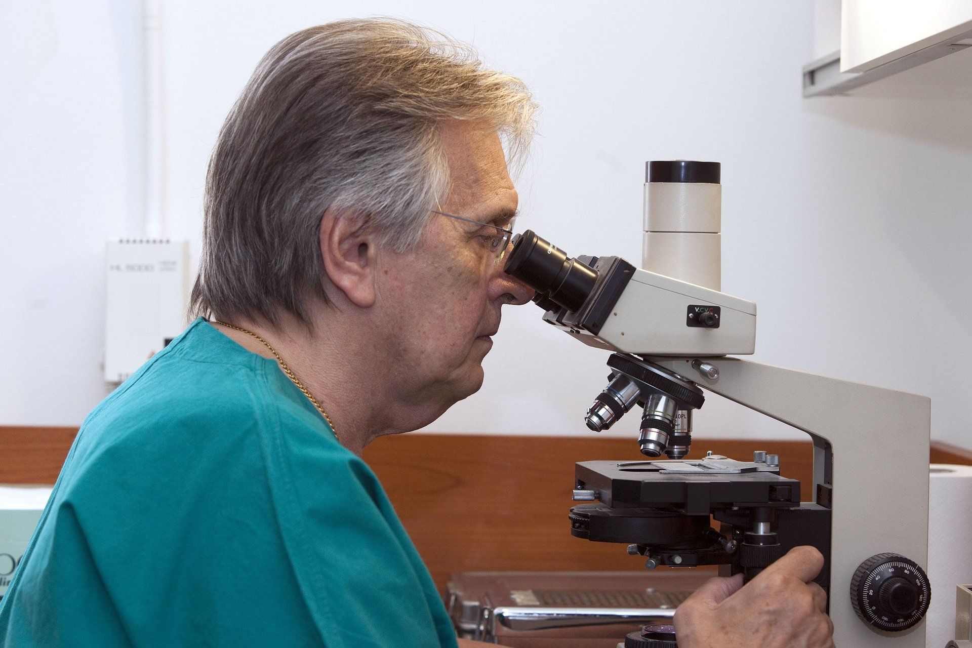 Uomo in camice verde che osserva un microscopio in un laboratorio.