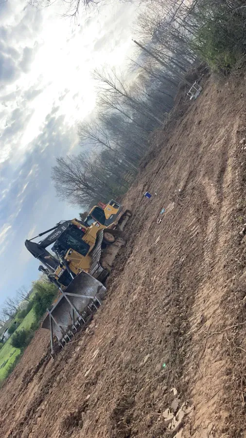 A yellow bulldozer on a dirt slope near a treeline under a cloudy sky.