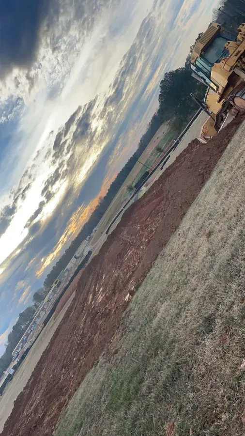 Bulldozer plowing a field under a cloudy, colorful sky; rural scene.