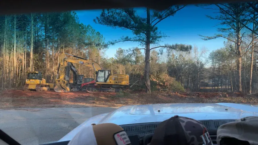 Excavators clearing trees in a forest. Viewed from inside a vehicle.