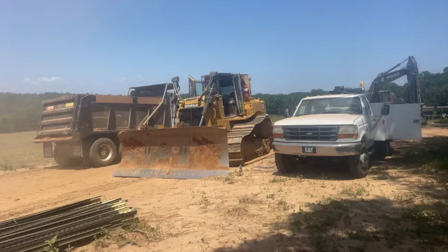 Yellow bulldozer, dump truck, and white pickup truck parked on dirt, outdoors.