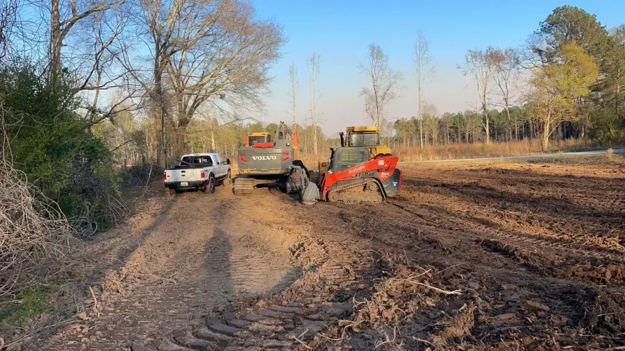 Two tractors and a truck on a dirt road next to a field.