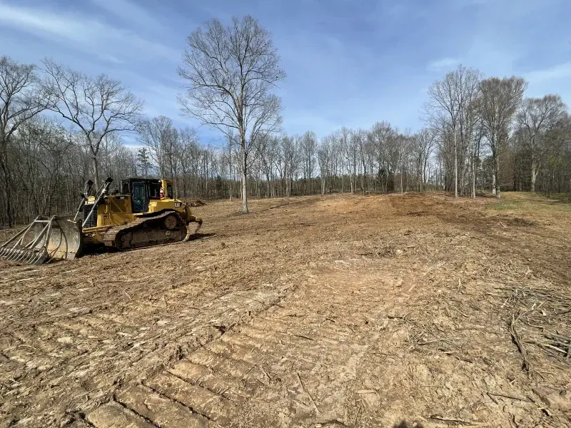 Bulldozer on a cleared plot of land, preparing a construction site among bare trees under a blue sky.