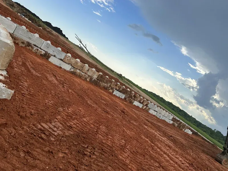 Red dirt and concrete blocks on a graded lot under a cloudy blue sky, likely for construction.