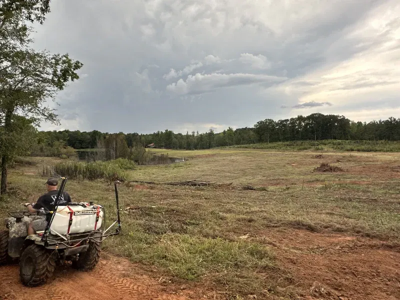 A person on an ATV sprays a field with a cloudy sky overhead.