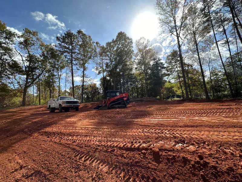 Cleared red earth with construction equipment and truck under sunny sky.