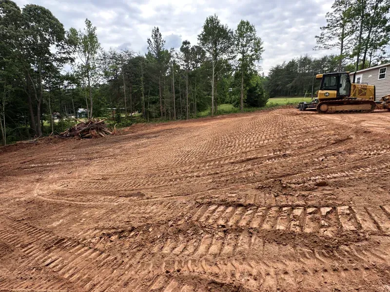Cleared red dirt lot with bulldozer, trees in background.