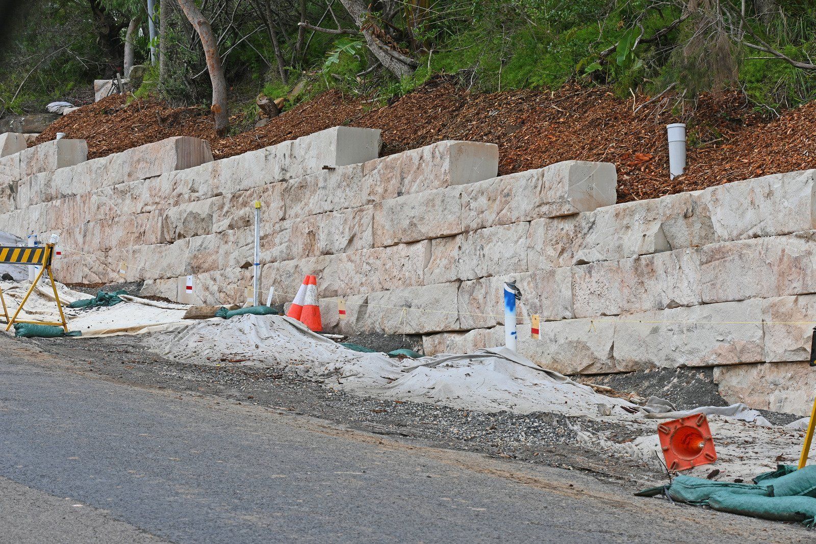 Stone retaining wall along a road. Construction area with orange cones and gravel.