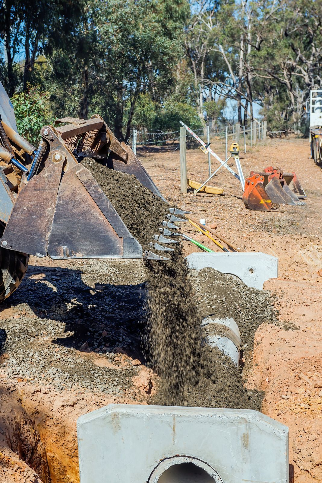 An excavator dumping gravel into a concrete structure in a ditch on a construction site.