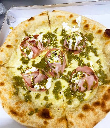 Pizza con formaggio fuso, salsa alle erbe aromatiche e fette di prosciutto cotto rosa arrotolato in una scatola bianca.