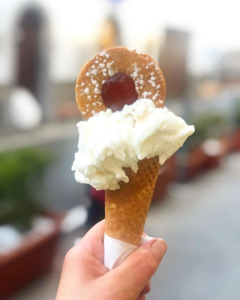 Mano che tiene un cono gelato sormontato da un biscotto a forma di anello e panna montata all'aperto