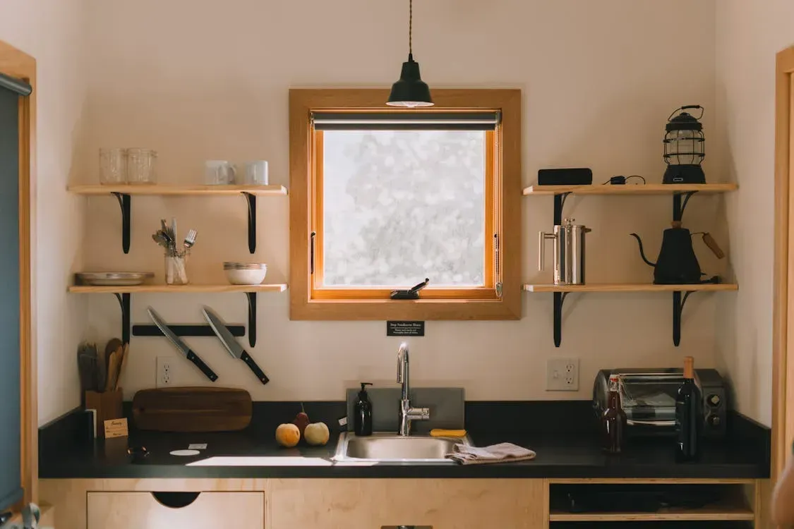 A kitchen with a sink , shelves , and a window.