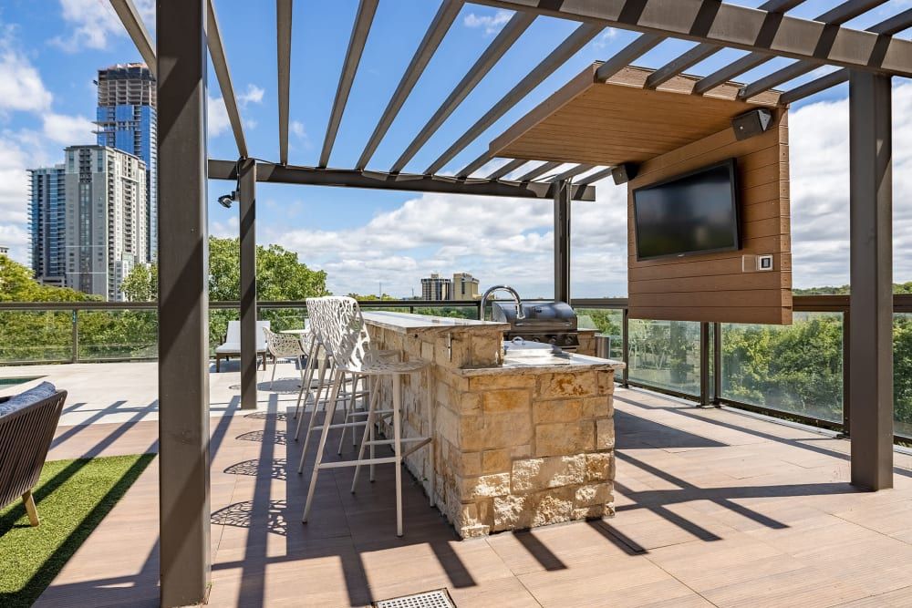 A rooftop deck with a bar , grill , television and a pergola at Water's Edge.